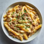 Close up of High Protein Beef Pasta in a white bowl showing the glossy light-orange cheese sauce and browned beef crumbles.