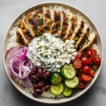Close up view of Greek Chicken Meal Prep Bowls with dark sear marks on chicken and creamy tzatziki.