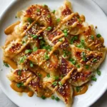 Golden-brown Oven-Baked Dumplings layered on a white ceramic rectangular plate with warm-tan peanut drizzle.