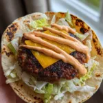 A handheld Smash Burger Taco showing the lacy charred beef edges and melted American cheese. (Smash Burger Tacos)