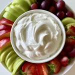 A close-up shot of a white ceramic bowl filled with glossy, thick Cream Cheese Fruit Dip showing soft rounded peaks and smooth texture.
