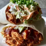 A close up handheld smartphone photo of two BBQ chicken wraps sliced in half and stacked on a white plate. (BBQ Chicken Coleslaw Wraps)