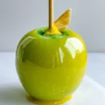 Handheld photo of a Pineapple Lemonade Candy Apple showing the translucent yellow coating and wooden dowel.