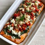 Handheld smartphone photo of Mediterranean Baked Salmon featuring flaky fish, dark green spinach, and vibrant red tomatoes. (Mediterranean Baked Salmon)