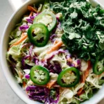 Jalapeño Slaw: The Ultimate Spicy Cilantro Lime Cabbage Salad Top-down close-up photo of fresh Jalapeño Slaw with green and purple cabbage and bright green jalapeño rounds in a white ceramic bowl.