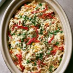 Summer Crockpot Recipes: Creamy Shredded Chicken with Garden Vegetables Top-down view of an oval ceramic slow cooker filled with shredded white meat chicken in a light creamy sauce with red peppers, green peas, and yellow corn. (Summer Crockpot Recipes)