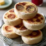 Close-up of five Homemade English Muffins with pale creamy dough and irregular golden toasted patterns on a stone countertop.