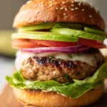 Eye-level shot of Juicy Ground Turkey Burgers on a wooden surface showing a dark brown seared crust and visible green herbs. (Juicy Ground Turkey Burgers)