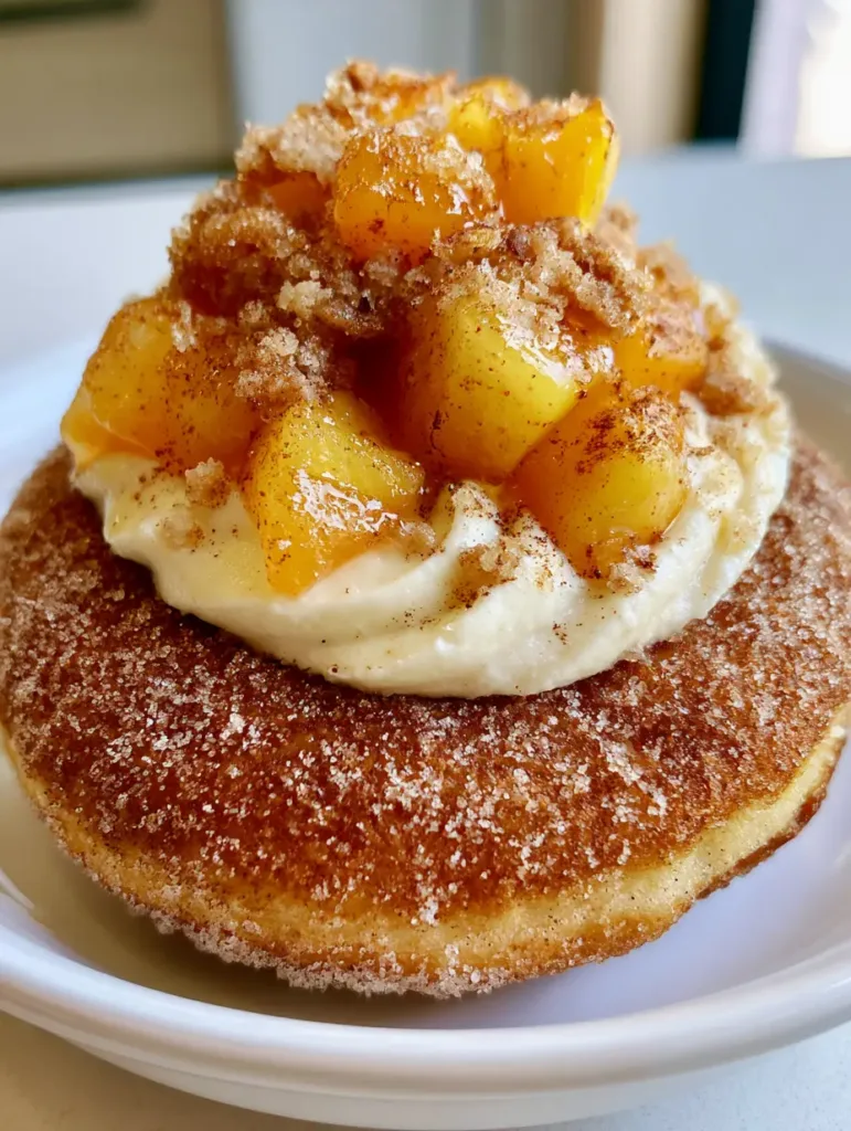 Side view of a Peach Cobbler Cheesecake Donut showing the visible flecks of cinnamon on the syrupy peaches.