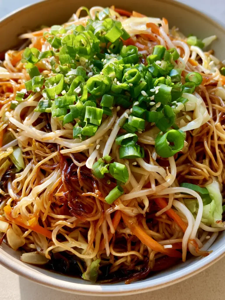 Overhead view of a ceramic bowl filled with glossy amber chow mein noodles and julienned carrots. (Easy Chow Mein Recipe)