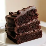 Midnight Fudge Cake with Glossy Dark Chocolate Frosting Close-up of a three-layer Midnight Fudge Cake showing the moist cocoa-brown spongy texture and spatula-textured frosting.