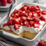 Handheld photo of a rectangular Strawberry Shortcake Sheet Cake showing the porous golden sponge and bright red berry slices.