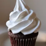 Handheld smartphone photo of a dark cocoa cupcake with voluminous Marshmallow Buttercream Frosting in natural daylight.