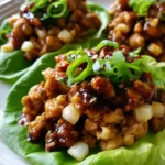 Three butter lettuce wraps on a white plate showing glossy dark amber hoisin chicken. (PF Chang's Chicken Lettuce Wraps)