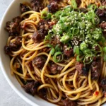 Asian Ground Beef Spaghetti: A 20-Minute Umami-Packed Fusion Dinner Top-down view of Asian Ground Beef Spaghetti showing the dark, translucent soy sauce and red chili oil flecks. (Asian Ground Beef Spaghetti)