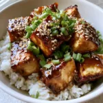 Close-up overhead shot of crispy Honey Garlic Tofu cubes with a dark amber glaze on white rice.