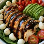 Baked Chicken Salad with Balsamic Glaze and Fresh Mozzarella Top-down view of a Baked Chicken Salad with diagonal chicken slices, mozzarella pearls, and halved cherry tomatoes.