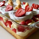 Strawberry Shortcake Banana Pudding Cake: The Ultimate Layered Summer Dessert A handheld photo showing the side view of a clear glass dish with layers of golden sponge, yellow pudding, red strawberries, and white cream. (Strawberry Shortcake Banana Pudding Cake)