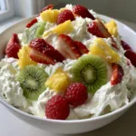 Hawaiian Cheesecake Salad: The Ultimate Tropical Fruit Fluff A white ceramic bowl filled with Hawaiian Cheesecake Salad, showing thick white cream, sliced strawberries, yellow pineapple, and green kiwi circles.