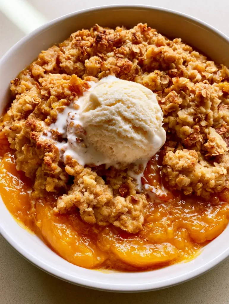 A close-up of bubbling Peach Cobbler with Oatmeal Crumble showing toasted oat flakes and syrupy peaches.