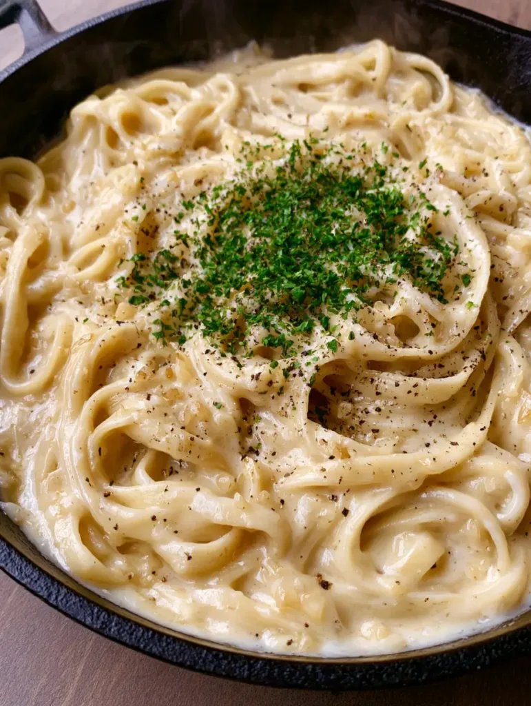 One Pot Creamy Garlic Pasta: A Silky 20-Minute Dinner Masterpiece 2 Handheld smartphone photo of one pot garlic pasta in a black skillet on a wooden surface with steam rising.