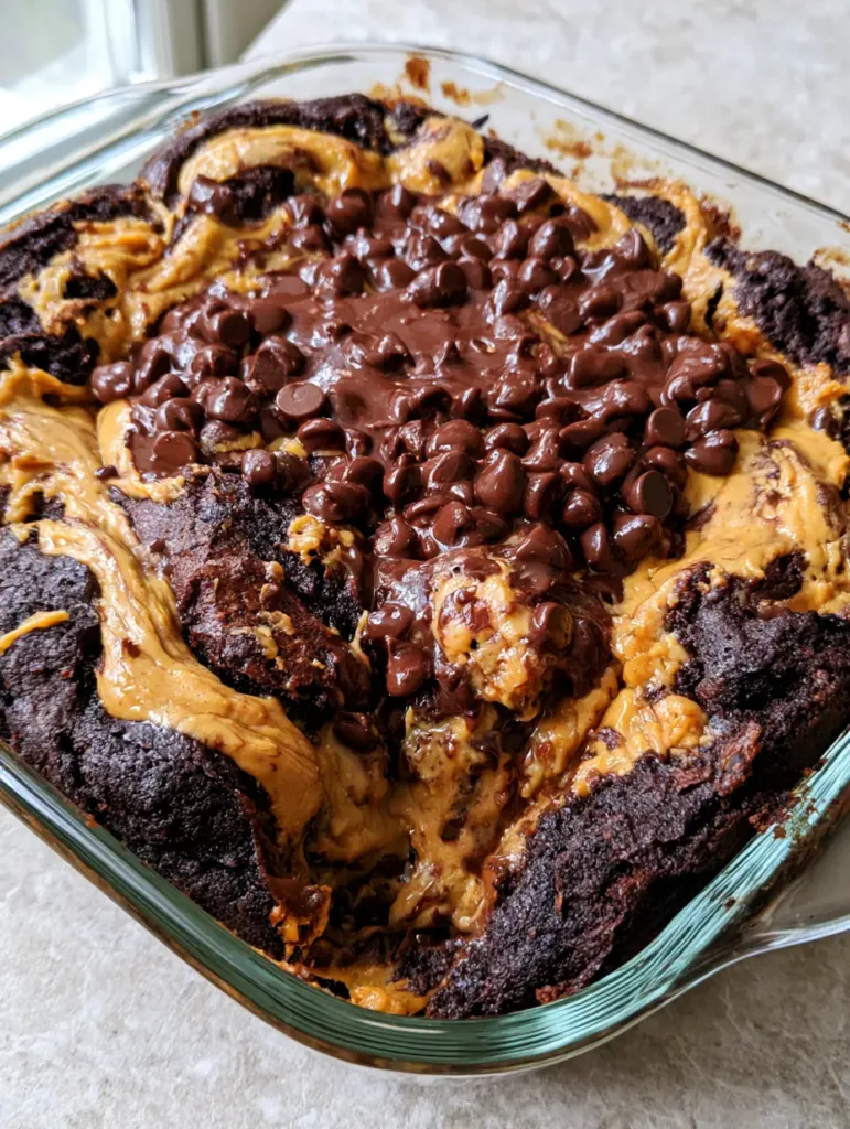 A close-up shot of a rectangular glass baking dish filled with a moist, dark chocolate cake base and creamy peanut butter swirls. (Chocolate Peanut Butter Dump Cake)