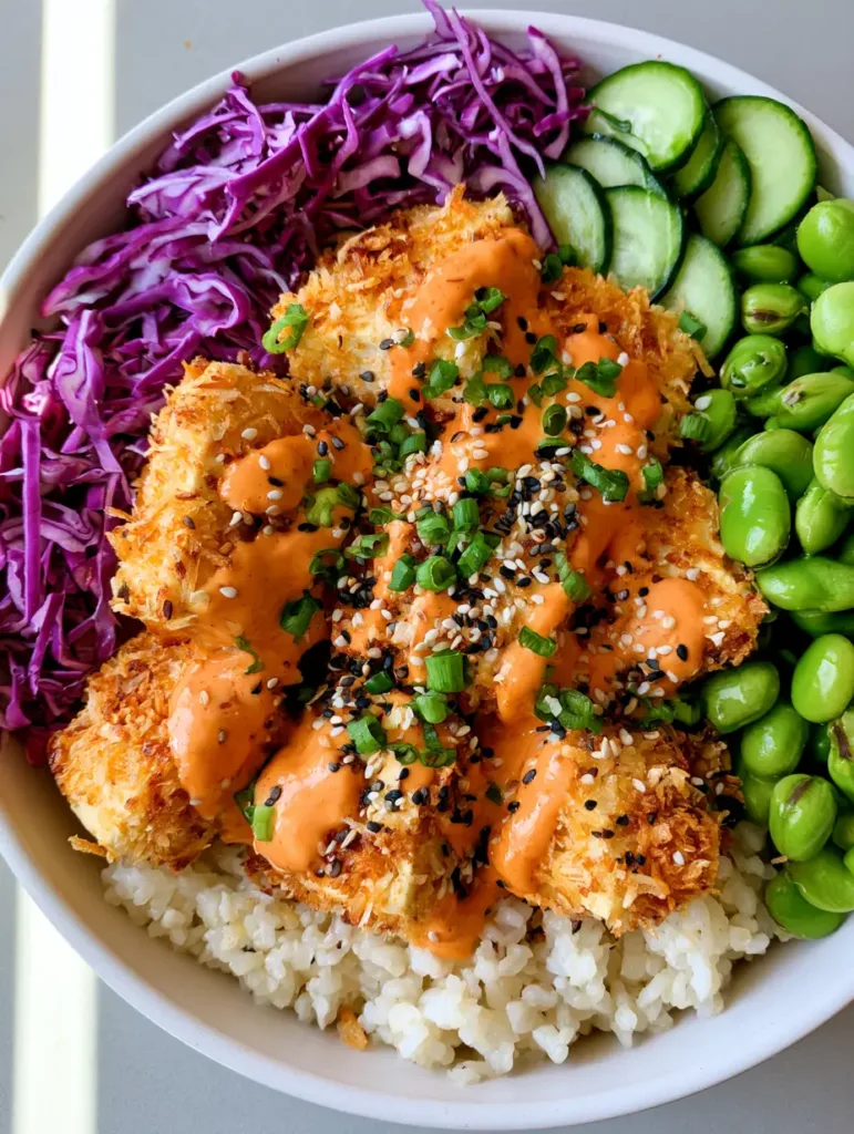 Close-up of golden-brown coconut-crusted tofu cubes drizzled with orange spicy mayo in a white bowl.
