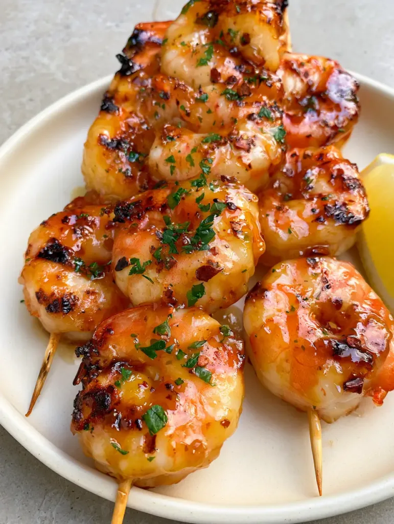 Stacked skewers of Grilled Shrimp Recipe garnished with red pepper flakes and parsley on a ceramic plate.