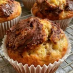 Top-down view of Nutella Banana Muffins on a wire cooling rack with visible banana bits and glossy Nutella swirls.