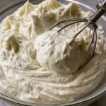Whipped mascarpone frosting in a glass bowl showing a smooth, velvety ivory texture and visible vanilla bean specks. (Mascarpone Frosting)