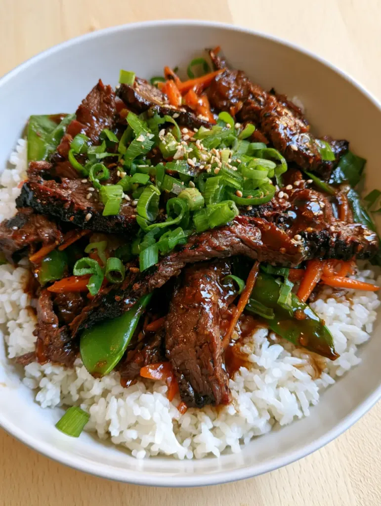 A shallow ceramic bowl of Chinese Beef Recipe stir fry showing the glossy dark brown glaze and fluffy jasmine rice foundation.