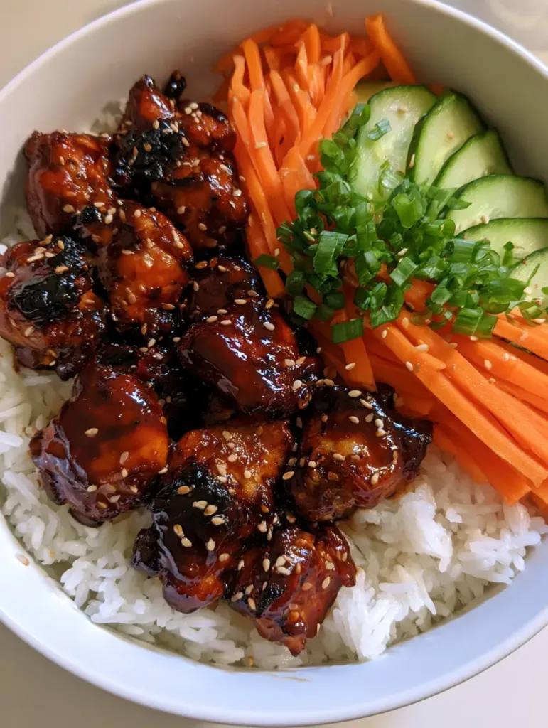 A close-up overhead shot of a white ceramic bowl filled with Korean BBQ Chicken Bowls showing charred chicken edges and glossy sauce.