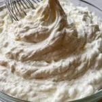 Close-up of thick, velvety white Chantilly cream in a glass bowl with black vanilla bean specks. (Chantilly Cream Recipe)