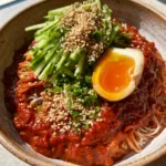 A handheld smartphone photo of Bibim Guksu in a rustic bowl on a stone countertop with a bright jammy yolk. (Bibim Guksu)