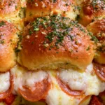Handheld smartphone photo of warm Hawaiian Roll Pizza Sliders on a baking sheet, showing golden crust and parsley flakes.