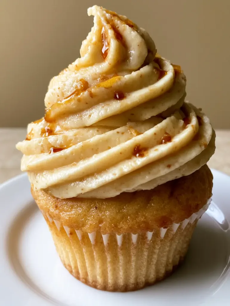 Close-up of a vanilla cupcake topped with thick Maple Buttercream Frosting and amber drizzle.