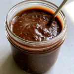 High-angle view of Creamy Balsamic Dressing in a mason jar on a concrete countertop with natural light highlights.