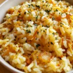 Close-up high-angle shot of Homemade Rice-A-Roni in an off-white ceramic bowl, glistening with butter and flecked with parsley.