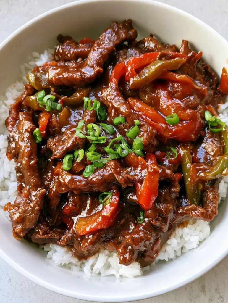 Close-up of Slow Cooker Pepper Steak in a white bowl showing the thick savory brown gravy and soft peppers. (Slow Cooker Pepper Steak)