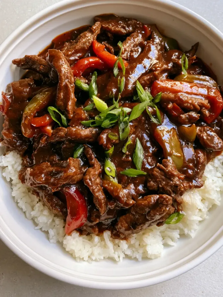 Top-down view of tender beef strips and green onions on a bed of rice. (Slow Cooker Pepper Steak)