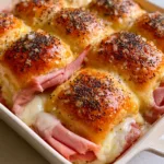 Close-up of toasted Hawaiian Ham and Cheese Sliders with glossy butter glaze, poppy seeds, and minced onions.
