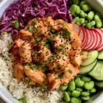 Close up shot of a Bang Bang Chicken Bowl with glossy light-orange sauce on bite-sized chicken and vibrant vegetable sections.