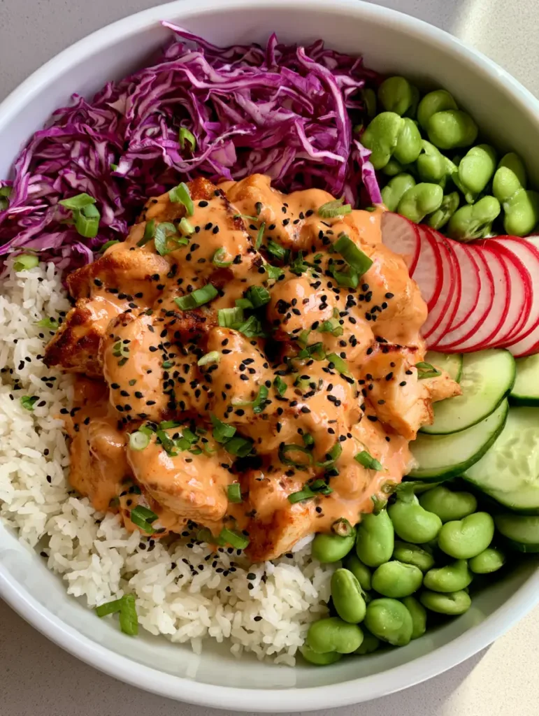Close up shot of a Bang Bang Chicken Bowl with glossy light-orange sauce on bite-sized chicken and vibrant vegetable sections.